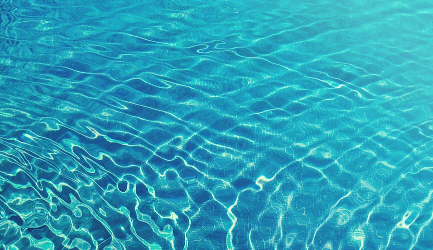A foto mostra uma piscina, mas o foco está somente na água, com uma luz do sol refletindo.