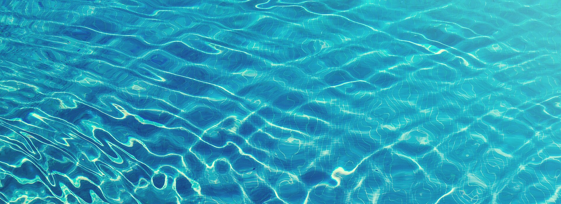A foto mostra uma piscina, mas o foco está somente na água, com uma luz do sol refletindo.