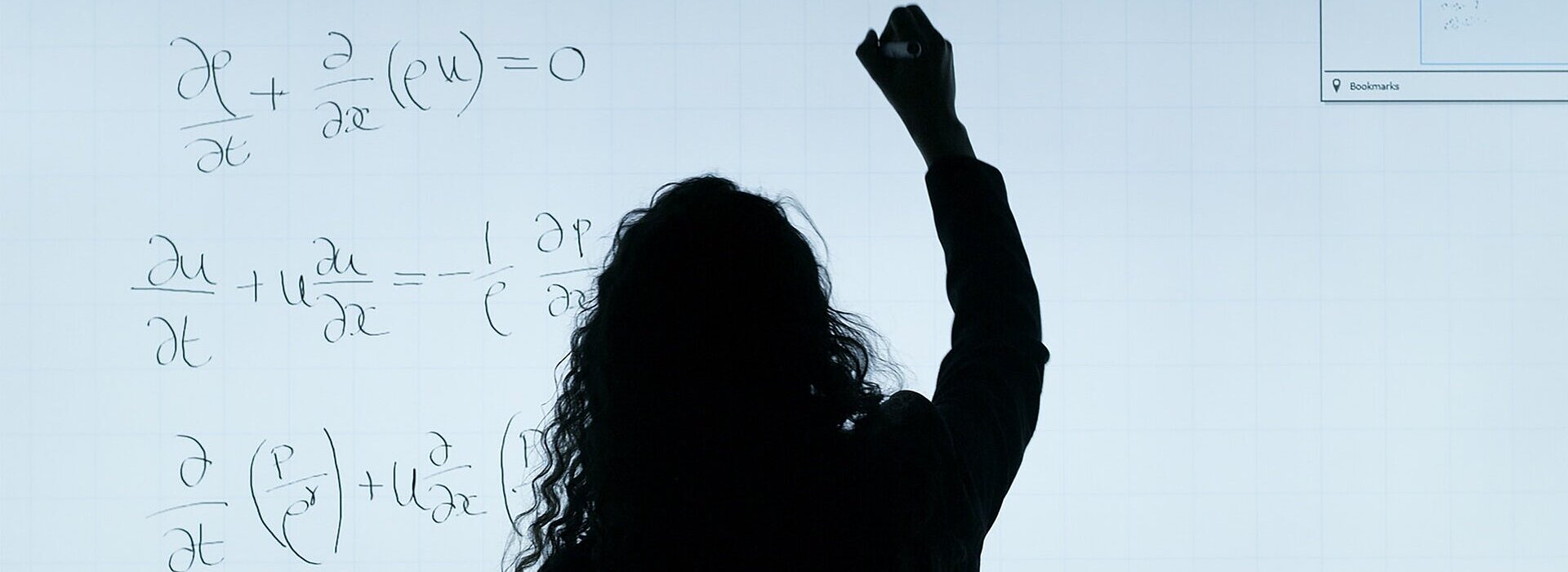Mulher de cabelos longos, de costas, escreve equações em uma lousa branca