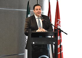 O pró-reitor está falando atrás de um pulpito, que tem o logo do Mackenzie.