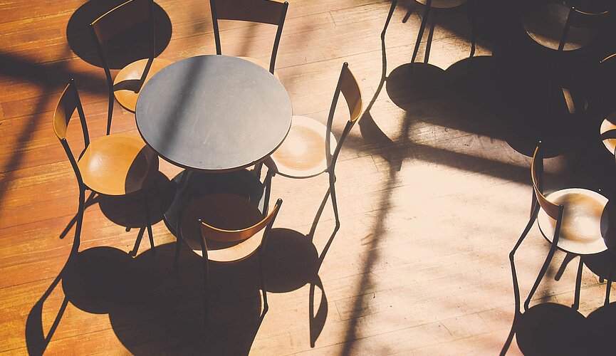 Na foto aparece resa redonda com várias cadeiras em volta. A foto foi tirada de cima e a luz do sol faz com que as cadeiras tenham uma sombra
