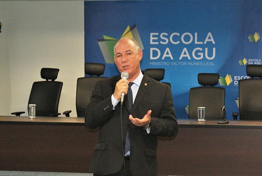 Walter Eustáquio em frente ao banner da AGU palestra na abertura do evento.