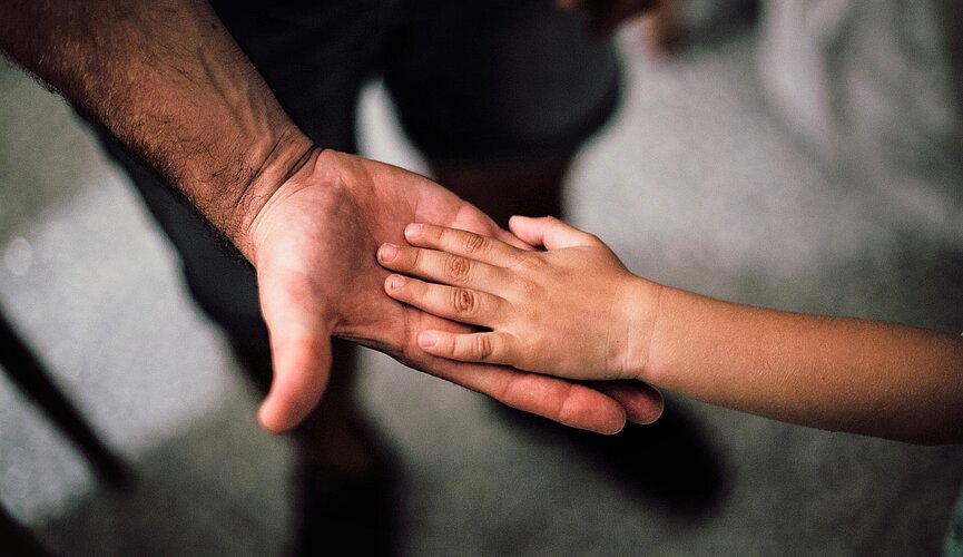 mão masculina de adulto apoia mão de criança numa imagem em close
