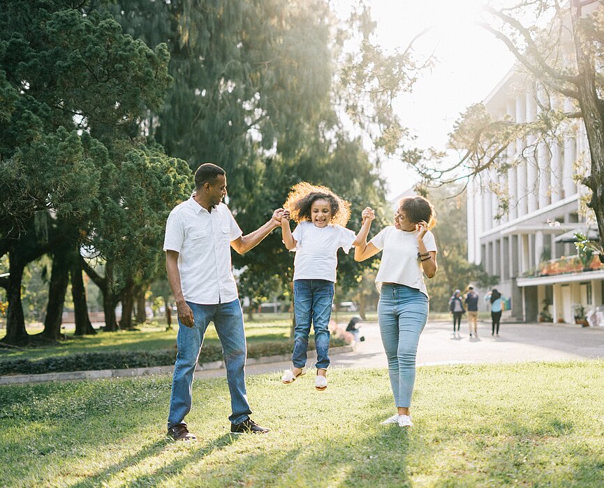 Criança pulando de mãos dadas com os pais
