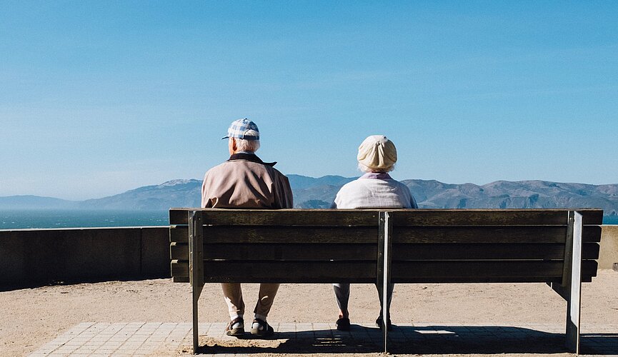 Idosos sentados em um banco e observando o horizonte. 