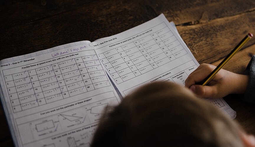 A foto foi tirada de cima e mostra uma pessoa fazendo uma prova.