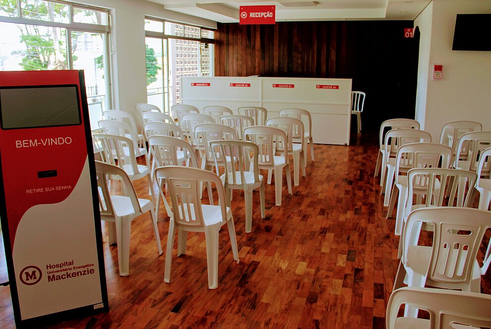 sala cheia de cadeiras, com totem de senhas e balcão de atendimento