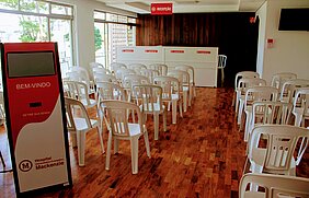 sala cheia de cadeiras, com totem de senhas e balcão de atendimento