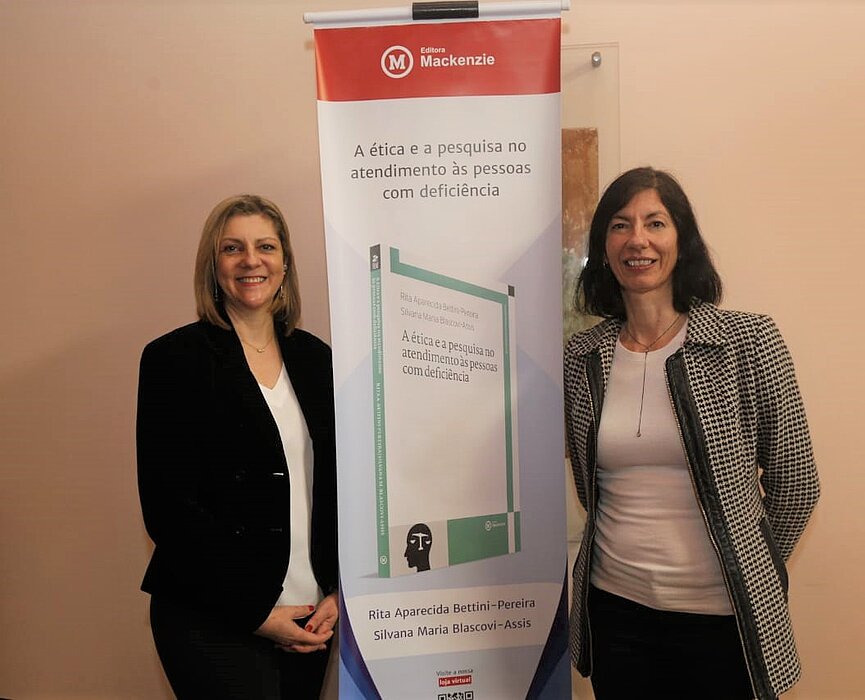 Autoras de pé ao lado do banner de apresentação do livro