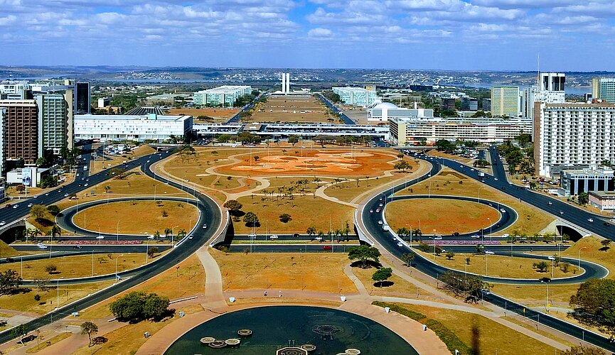 imagem do alto do planalto, em Brasília. o céu está azul, com algumas poucas nuvens brancas e pode-se ver os prédios, ruas e praças
