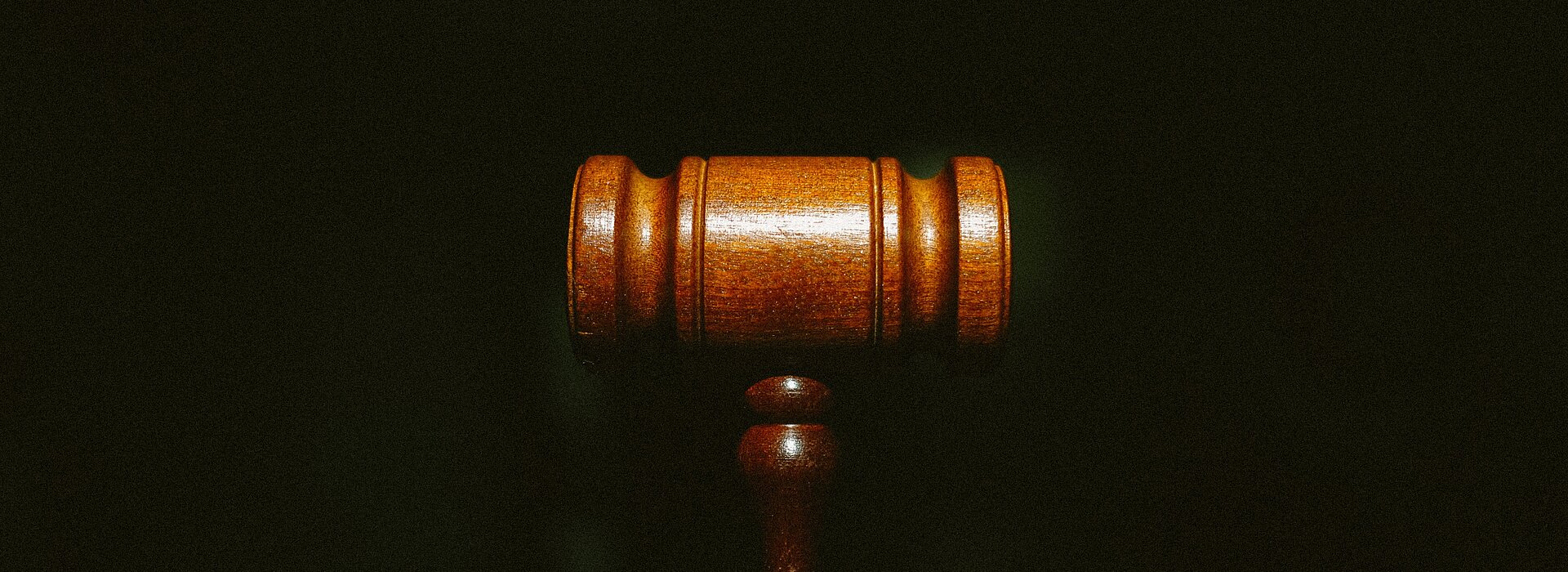 Na foto um malhete marrom, o famoso martelo utilizado pelo juiz, está centralizado no meio. O fundo é todo escuro e o foco está somente no martelo.