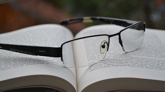 Imagem com um livro aberto e um óculos de grau em cima