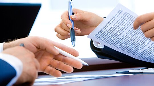 Mãos segurando canetas com documentos sobre a mesa