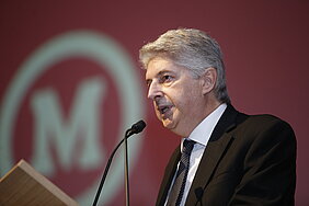 Professor Morsch ao púlpito com fundo vermelho com símbolo do Mackenzie