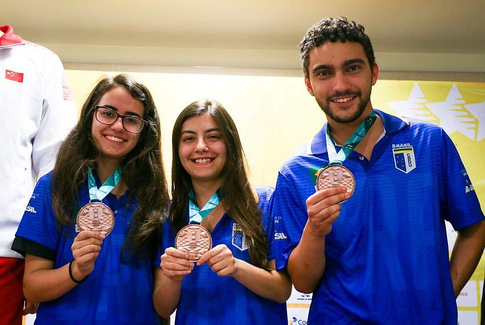 Três atletas de uniforme azul posam para foto com suas medalhas de terceiro lugar