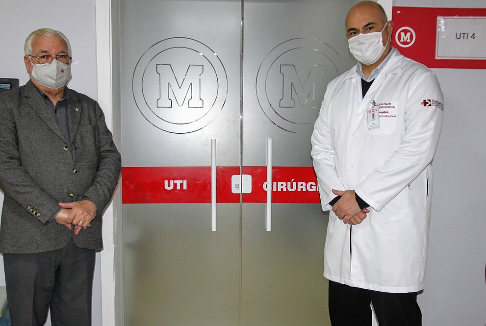Dois homens de máscara em pé em frente às portas do novo centro cirúrgico hospitalar
