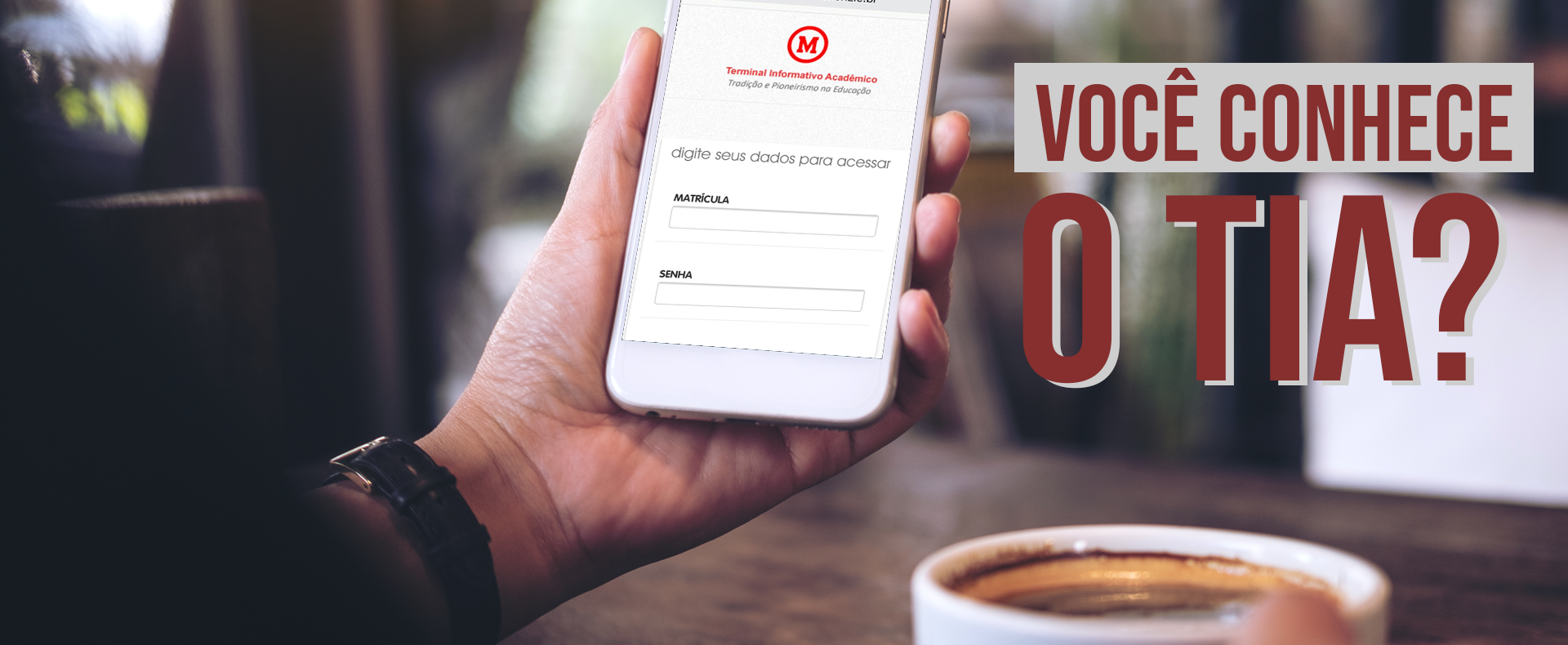 A foto mostra o braço e a mão de um homem usando um relógio segura um celular que aparece a página do aplicativo do TIA. Na mesa na qual ele está se apoiando tem um xícara de café