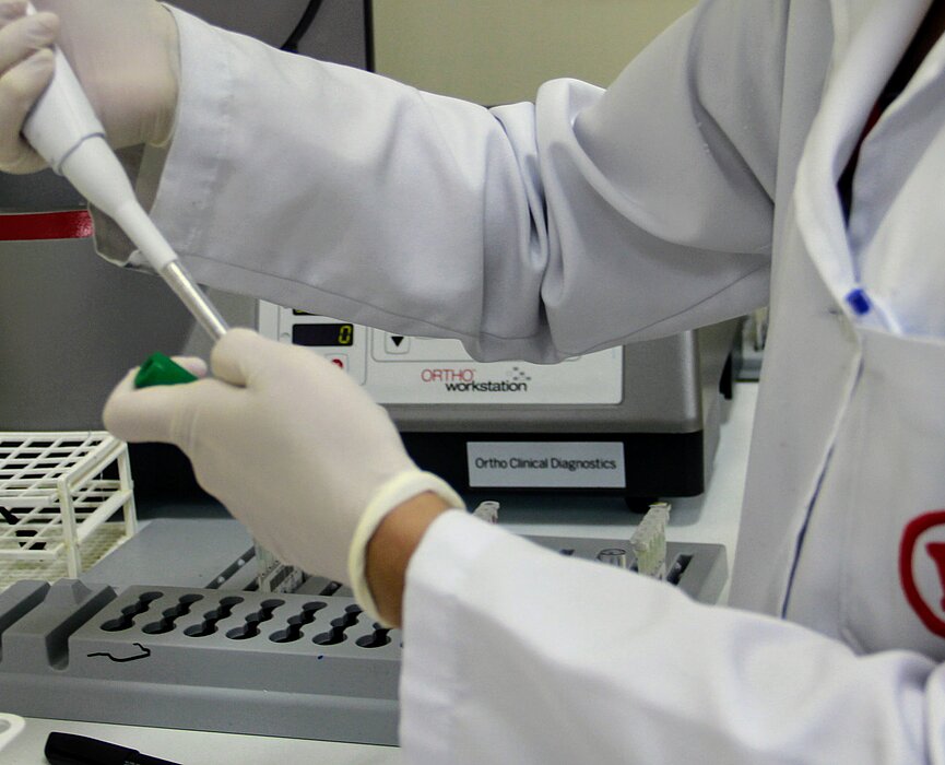 profissional de laboratório com jaleco branco com símbolo do Mackenzie em vermelho, manipulando uma pipeta de laboratório