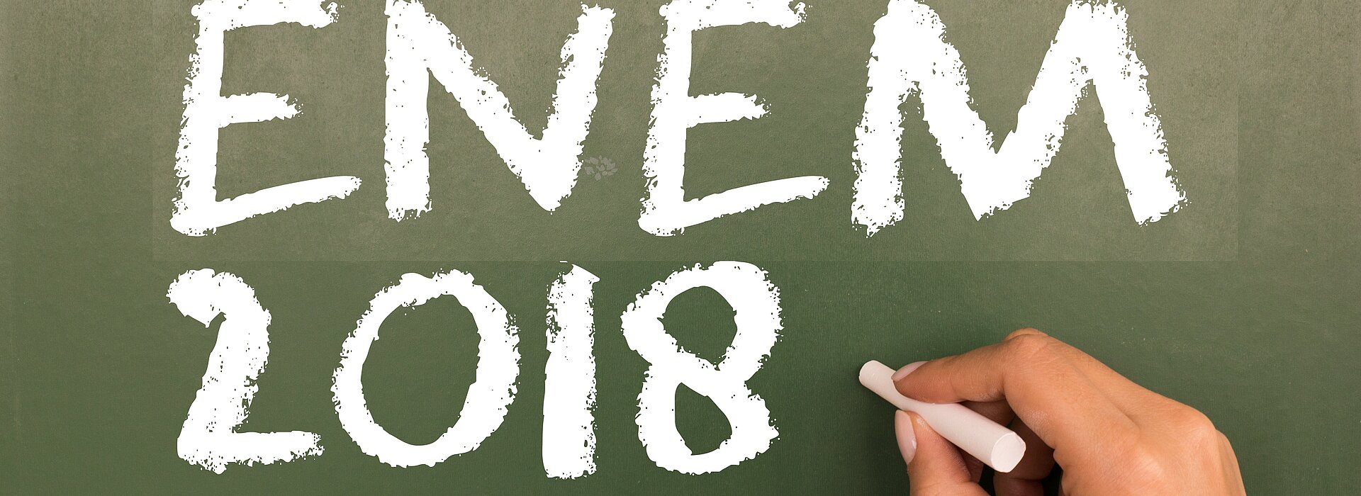 Mão segurando giz com a inscrição "Enem 2018" no quadro negro