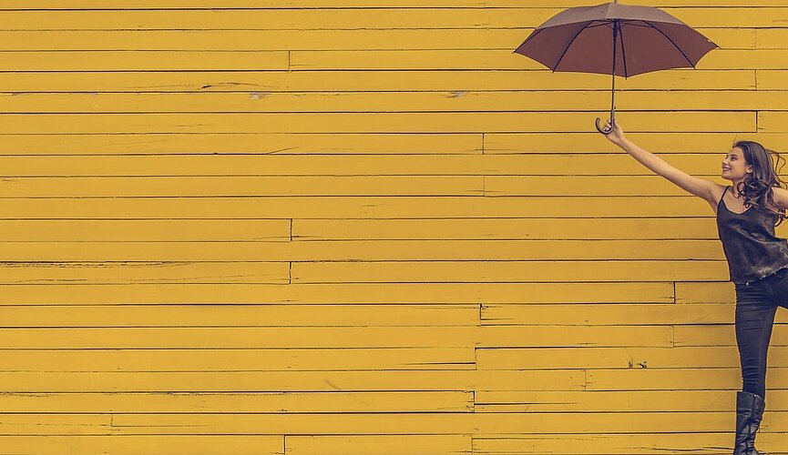 mulher segurando um guarda-chuva e pulando em um fundo de parede amarela