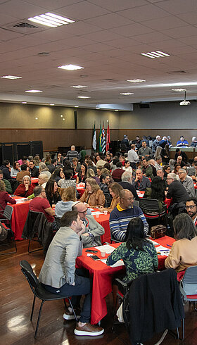 Imagem tirada do "XI Fórum de Aprendizagem Transformadora" e nela contem um auditório cheio pessoas sentadas debatendo.