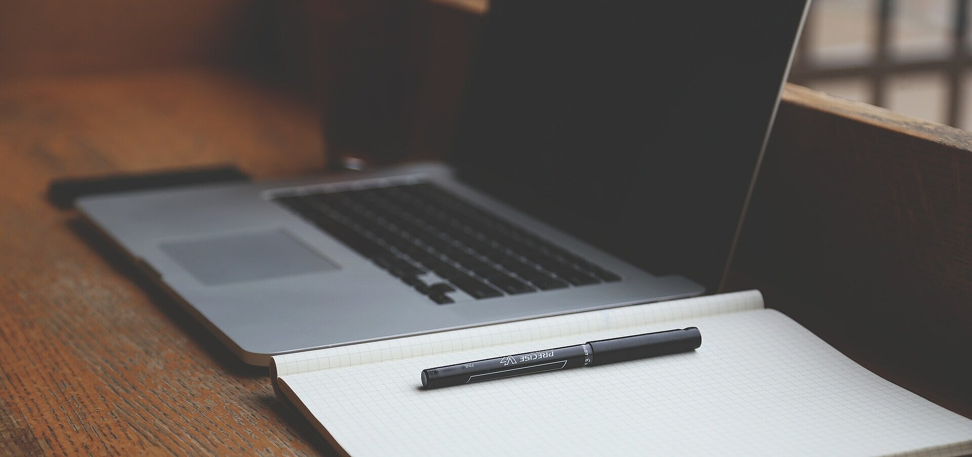 Notebook ao lado de caderno, ambos em cima da mesa.