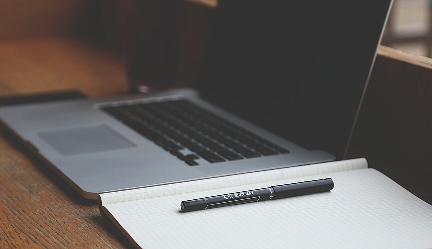 Notebook ao lado de caderno, ambos em cima da mesa.