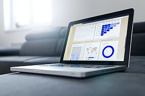 laptop sobre uma mesa cinza, na tela, há gráficos e dados variados