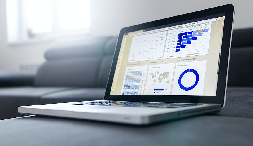 laptop sobre uma mesa cinza, na tela, há gráficos e dados variados