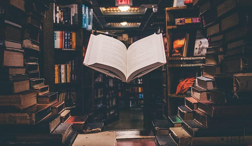 livro aberto em meio a uma biblioteca