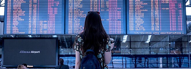 Garota olhando tela de desembarque em aeroporto.