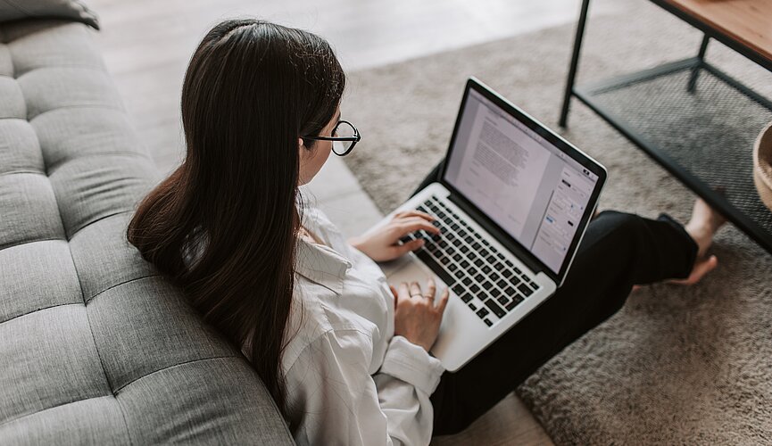 Estudante sentada no chão e mexendo em seu notebook 