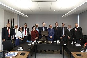 12 pessoas de pé atrás de mesas de reunião posando para foto