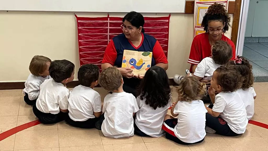 Duas professoras do Colégio Mackenzie lendo livro de histórias para uma roda de alunos em idade infantil